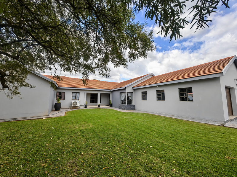 A well-maintained rear exterior view of the house featuring a spacious lawn, terracotta tiled roof, and paved pathways.