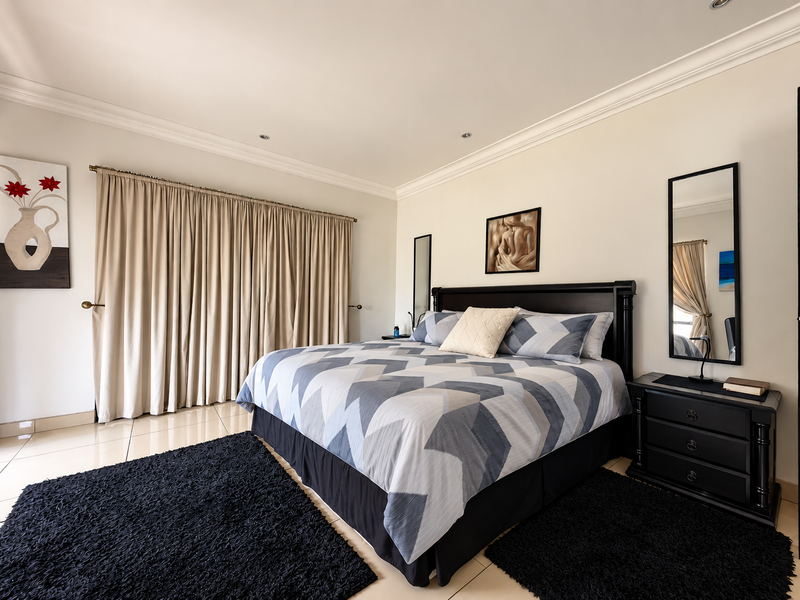 A well-maintained bedroom featuring neutral walls, crown molding, recessed lighting, and tiled flooring, providing a clean and comfortable living space.