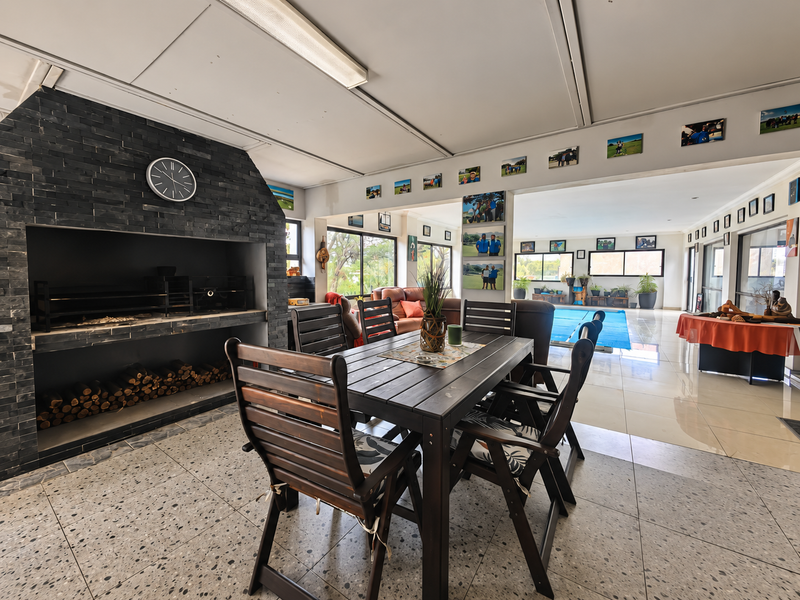 Spacious covered patio featuring a built-in stone-clad braai, tiled flooring, and direct access to the pool area.