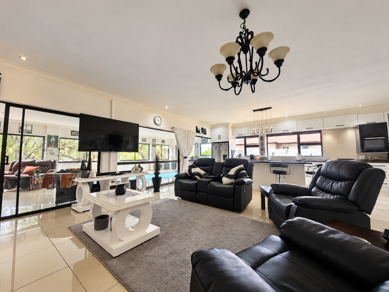 Spacious open-plan living area featuring polished floor tiles, a modern kitchen with integrated appliances, and large sliding doors leading to the outdoor pool area.
