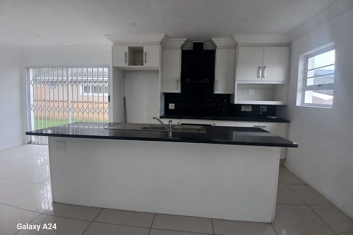 Modern open-plan kitchen featuring a central island, sleek white cabinetry, black countertops, and tiled flooring with direct access to the outdoor area.