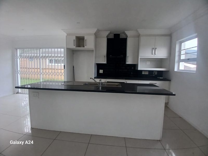 Modern open-plan kitchen featuring a central island, sleek white cabinetry, black countertops, and tiled flooring with direct access to the outdoor area.
