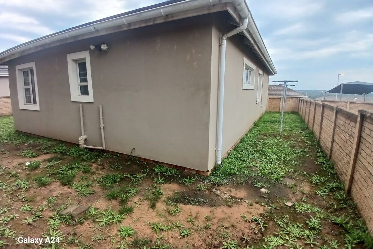 Rear exterior view of the townhouse featuring a side yard with boundary walling, guttering, and downpipes, requiring landscaping and exterior maintenance.