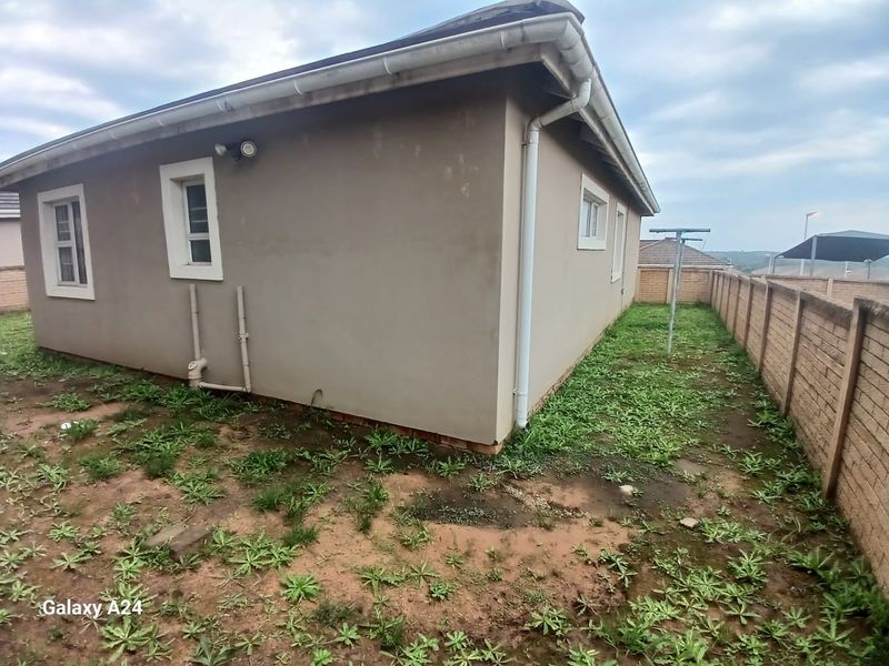 Rear exterior view of the townhouse featuring a side yard with boundary walling, guttering, and downpipes, requiring landscaping and exterior maintenance.