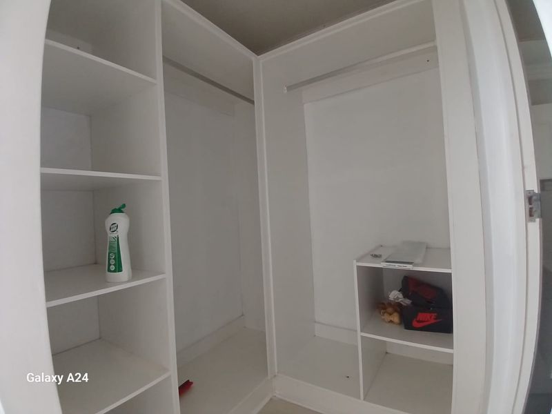 A walk-in closet or bedroom wardrobe featuring white built-in shelving and hanging rails, providing ample storage space.
