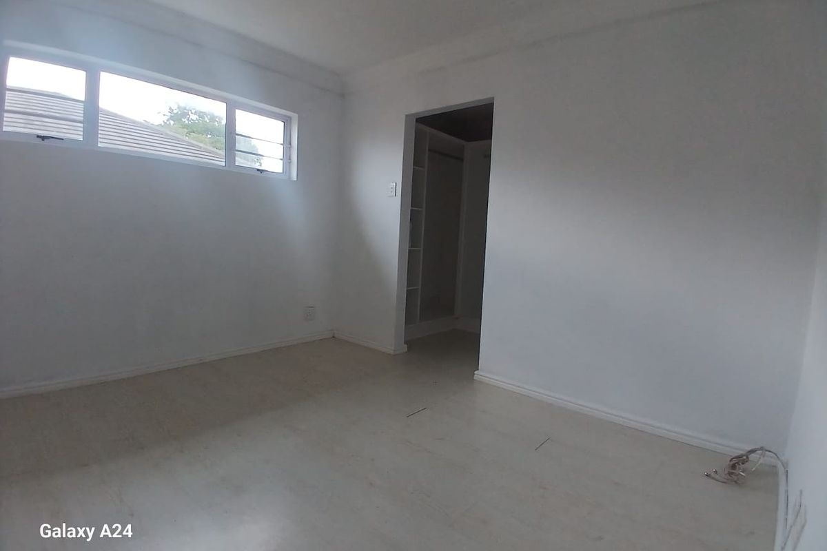 An empty bedroom featuring laminate flooring, a horizontal window, and an adjoining walk-in wardrobe area with built-in shelving.