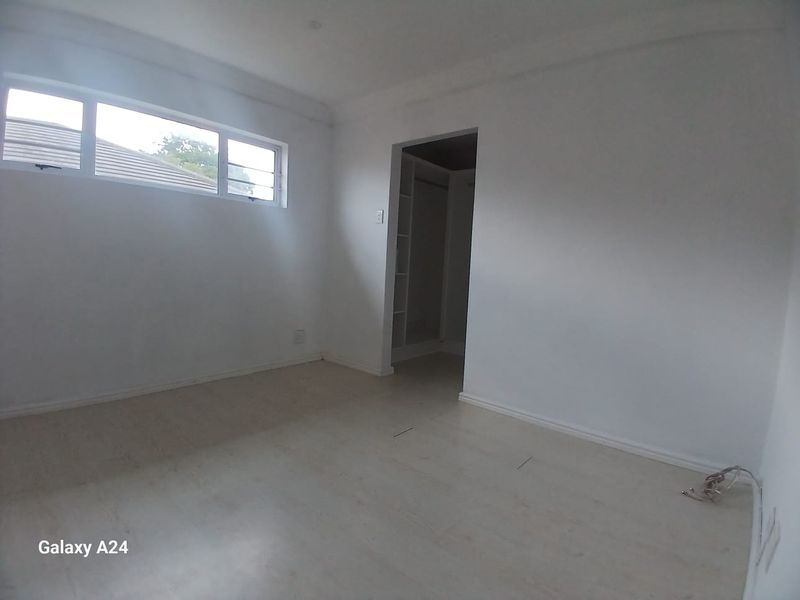 An empty bedroom featuring laminate flooring, a horizontal window, and an adjoining walk-in wardrobe area with built-in shelving.