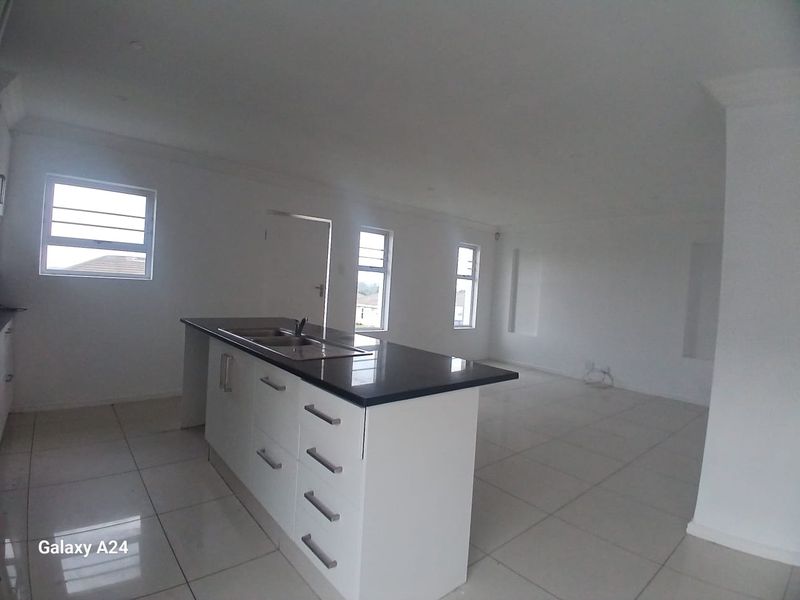 Spacious open-plan living area featuring a modern kitchen island with a dark countertop, tiled flooring, and ample natural light from multiple windows.