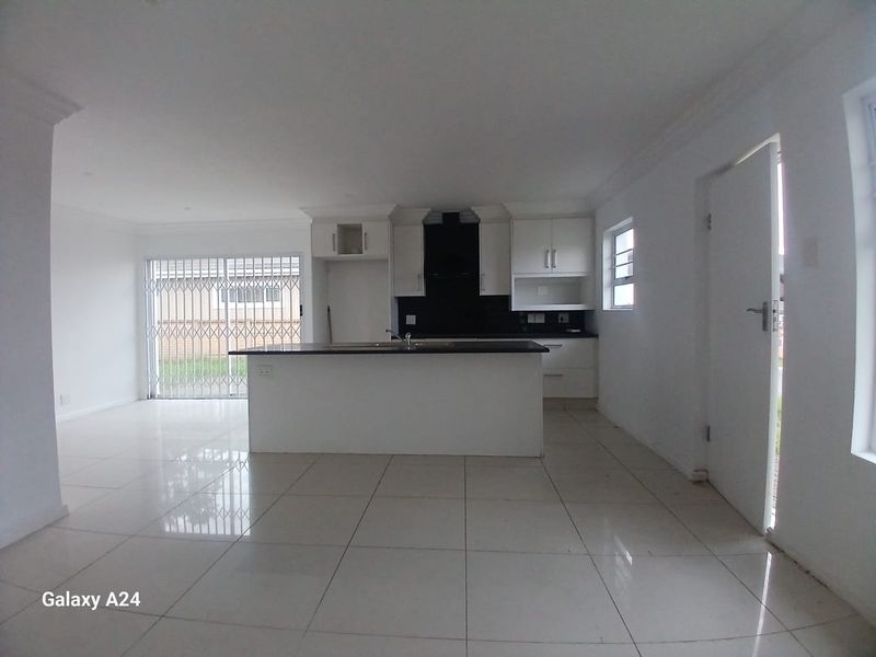An open-plan kitchen and living area featuring modern white cabinetry, a central island, and tiled flooring, presented in a clean, vacant state.