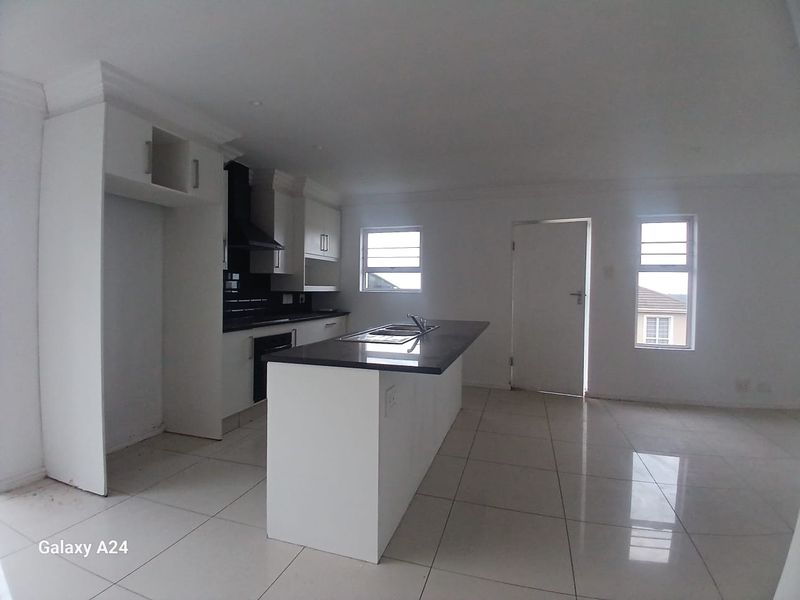An open-plan kitchen and living area featuring a central island, modern cabinetry, built-in oven, extractor fan, and neutral tiled flooring throughout.