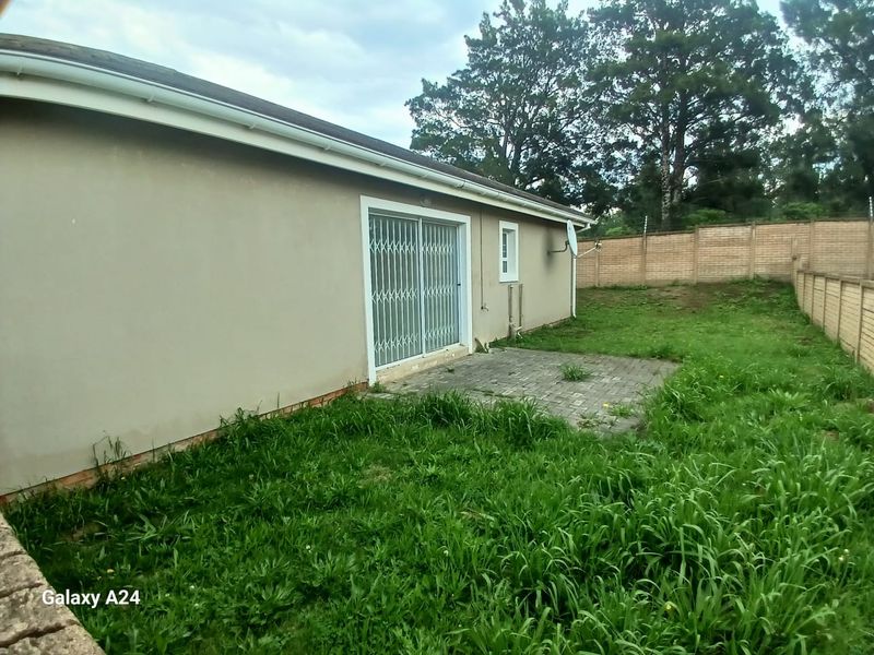 Rear exterior view of the townhouse featuring a paved patio area, sliding door with security gate, and a large, overgrown garden space.
