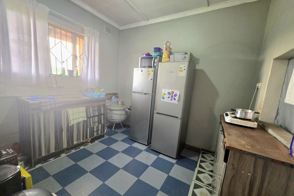 A functional kitchen space featuring a sink, tiled flooring, and security bars on the window, currently requiring cosmetic updates to improve its overall condition.