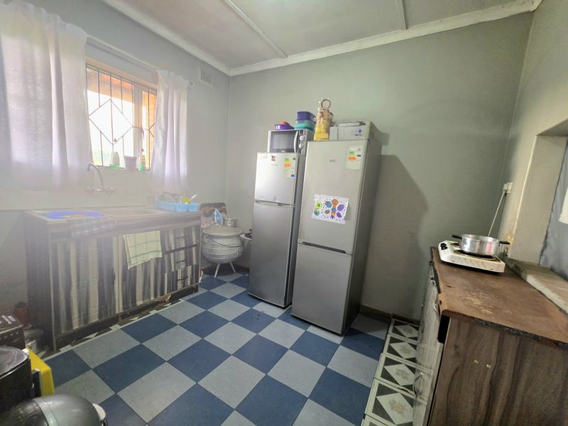 A functional kitchen space featuring a sink, tiled flooring, and security bars on the window, currently requiring cosmetic updates to improve its overall condition.