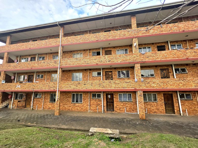 A multi-story apartment building exterior featuring face brick construction, paved ground level access, and security gates on individual unit entrances.