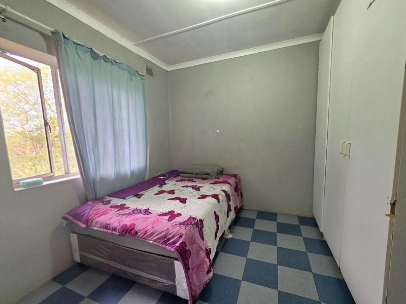 A functional bedroom featuring built-in cupboards, tiled flooring, and a window providing natural light.