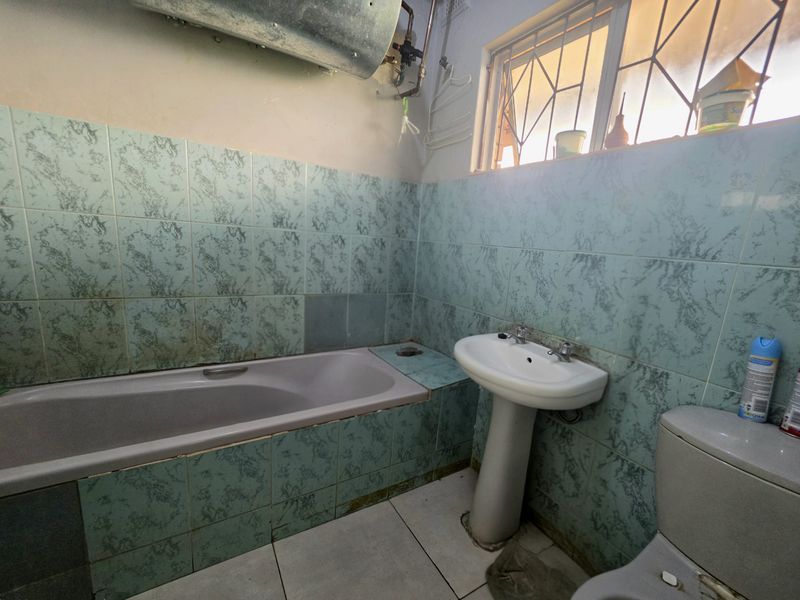 A dated bathroom featuring a pedestal basin, bathtub, and toilet with original tiled finishes, requiring modernization and cosmetic updates.