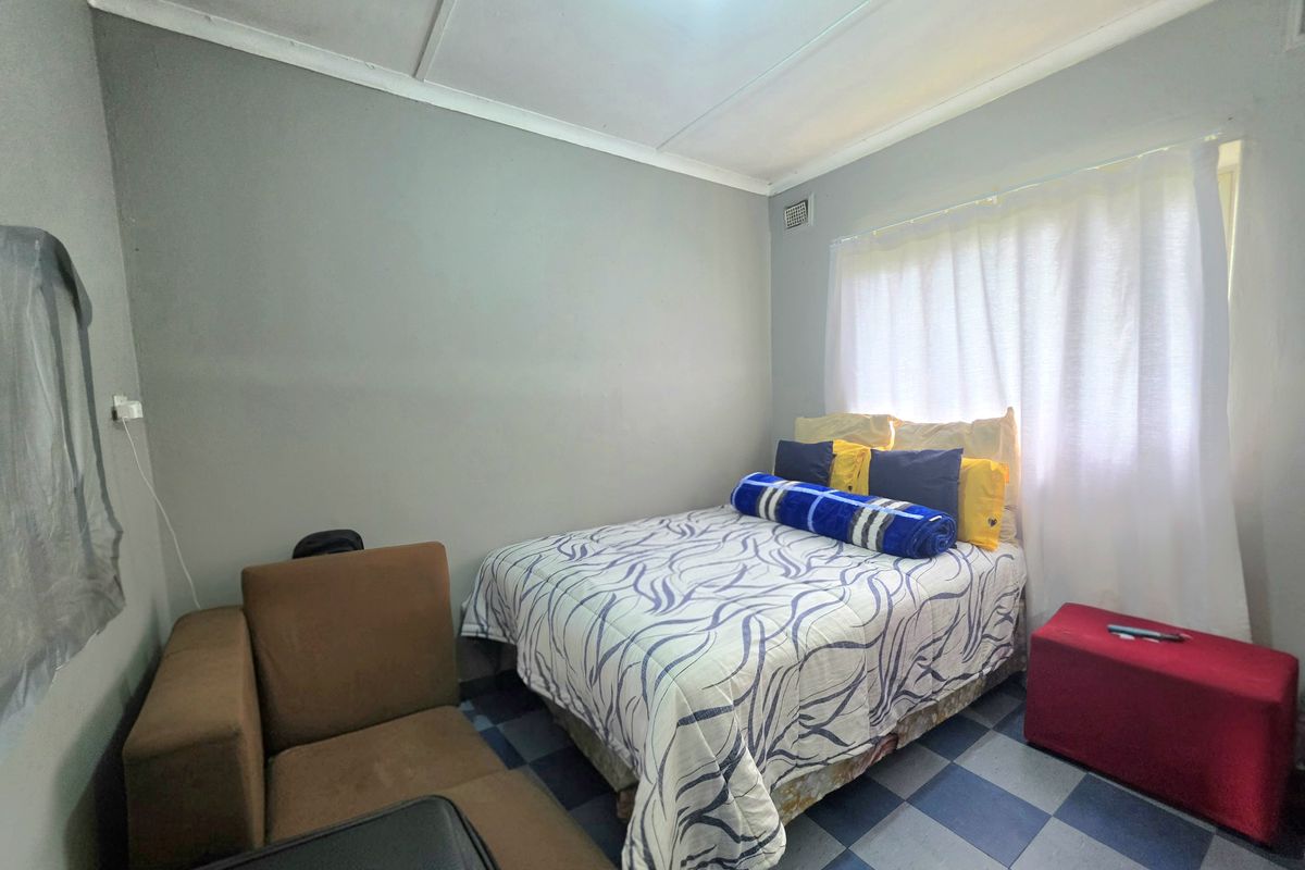 A compact bedroom featuring tiled flooring and neutral wall finishes, offering a functional space that could benefit from modern updates and improved lighting.