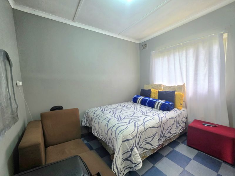 A compact bedroom featuring tiled flooring and neutral wall finishes, offering a functional space that could benefit from modern updates and improved lighting.