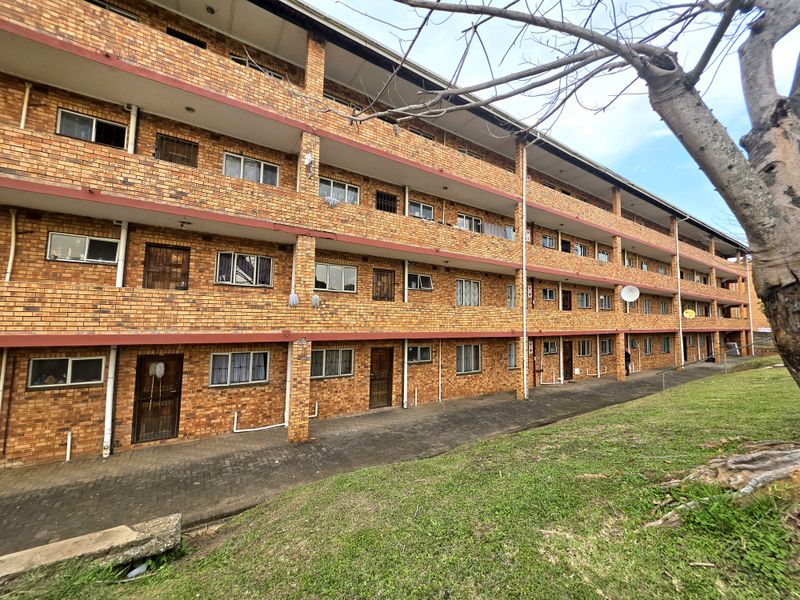 A multi-story apartment building featuring a face brick facade, paved ground-level walkways, and security-fitted entrances for each unit.