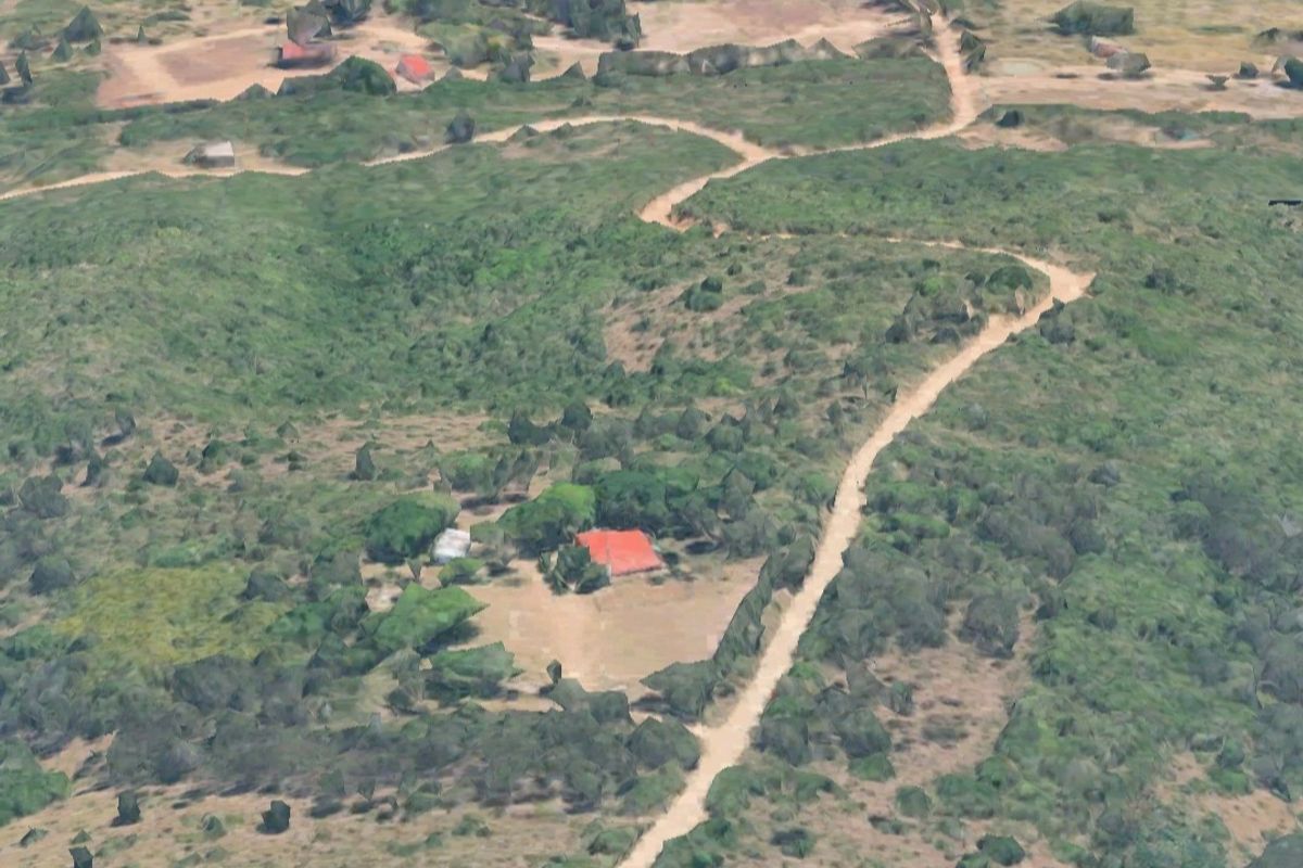 Aerial view of a small holding property featuring a main dwelling with a red roof, surrounded by natural landscape and accessible via a dirt road.