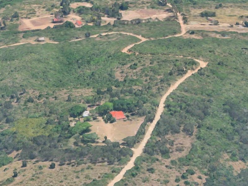 Aerial view of a small holding property featuring a main dwelling with a red roof, surrounded by natural landscape and accessible via a dirt road.