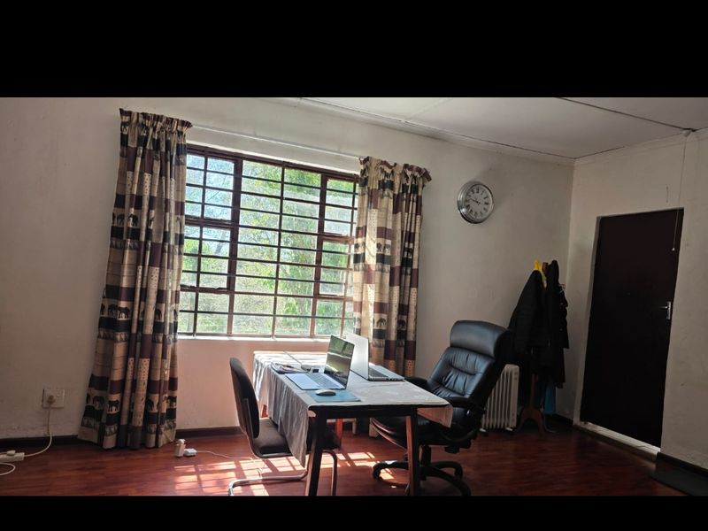 A functional home office space featuring laminated flooring, a large steel-framed window, and a solid core door, offering a quiet workspace environment.
