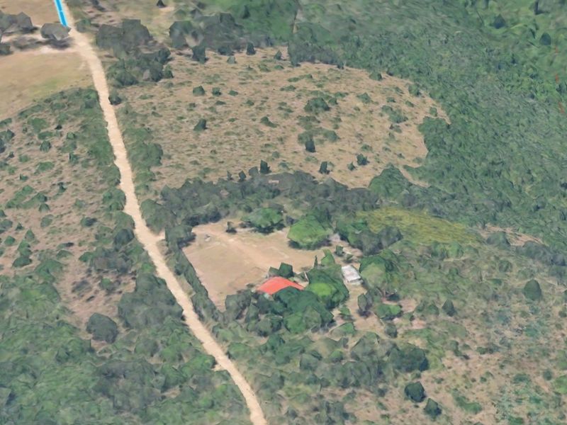 Aerial view of a rural small holding property featuring a main dwelling with a red roof, outbuildings, and access via a dirt road.
