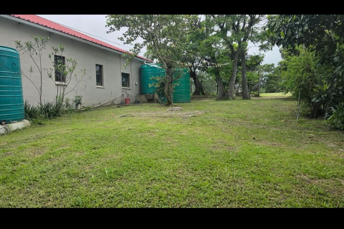 A spacious rear garden area featuring established trees, a lawn, and multiple water storage tanks adjacent to the main dwelling.