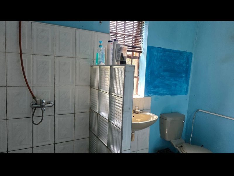 A functional bathroom featuring a shower area with glass block partition, wall-mounted basin, and toilet, requiring cosmetic updates to finishes.