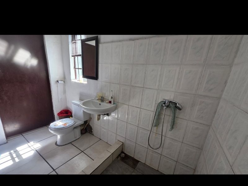 A functional bathroom featuring tiled walls and flooring, a wall-mounted basin, and a shower mixer, requiring cosmetic updates to improve its condition.