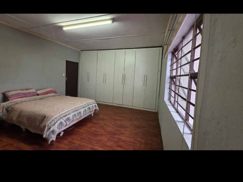 Spacious bedroom featuring built-in cupboards, laminate flooring, and large windows with security bars, offering a functional and well-lit living space.