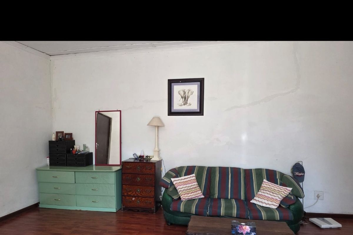 A living room area featuring laminate flooring and plain walls with visible signs of wear and cracking.