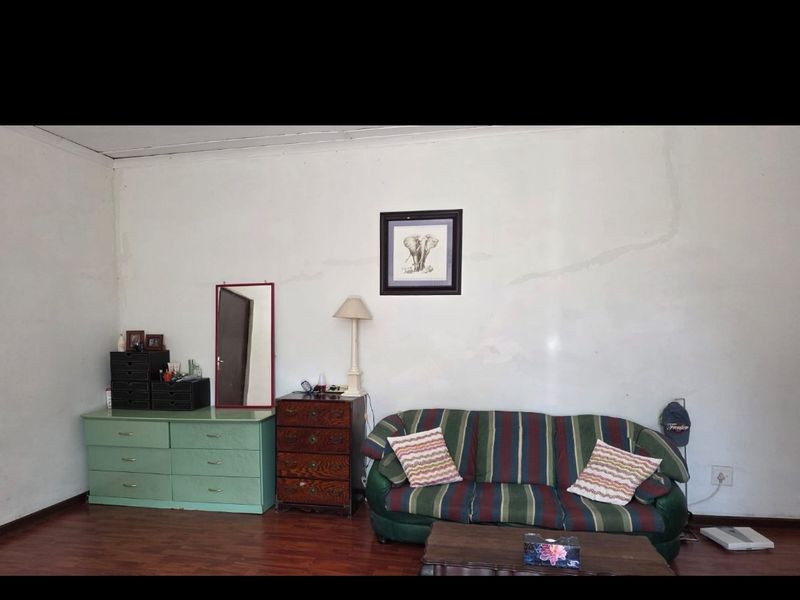 A living room area featuring laminate flooring and plain walls with visible signs of wear and cracking.