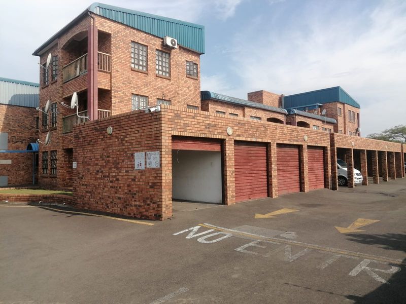 Exterior view of a multi-story face brick apartment complex featuring a row of garages and balconies under a metal roof structure.