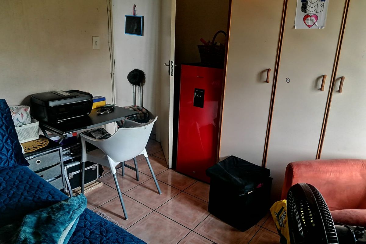 A bedroom featuring built-in cupboards and tiled flooring, currently used as a multi-purpose living and workspace area.