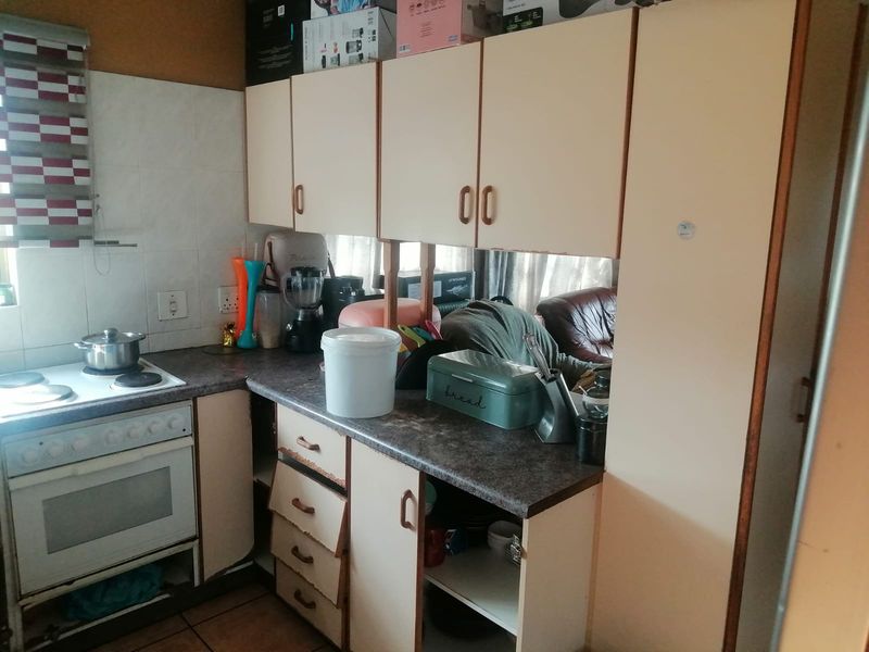 A compact kitchen featuring dated built-in cabinetry, laminate countertops, and an integrated electric stove and oven, requiring cosmetic updates.
