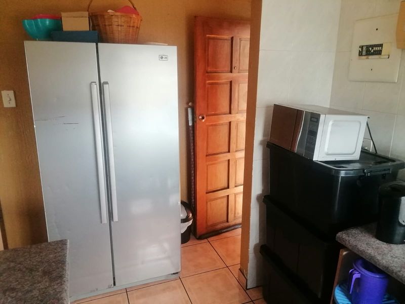 A kitchen area featuring tiled flooring, a timber door, and an exposed electrical distribution board, currently used for storage and appliance placement.