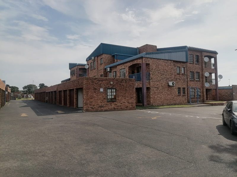 Exterior view of a multi-story face brick apartment complex featuring a row of garages, paved driveway, and private balconies.