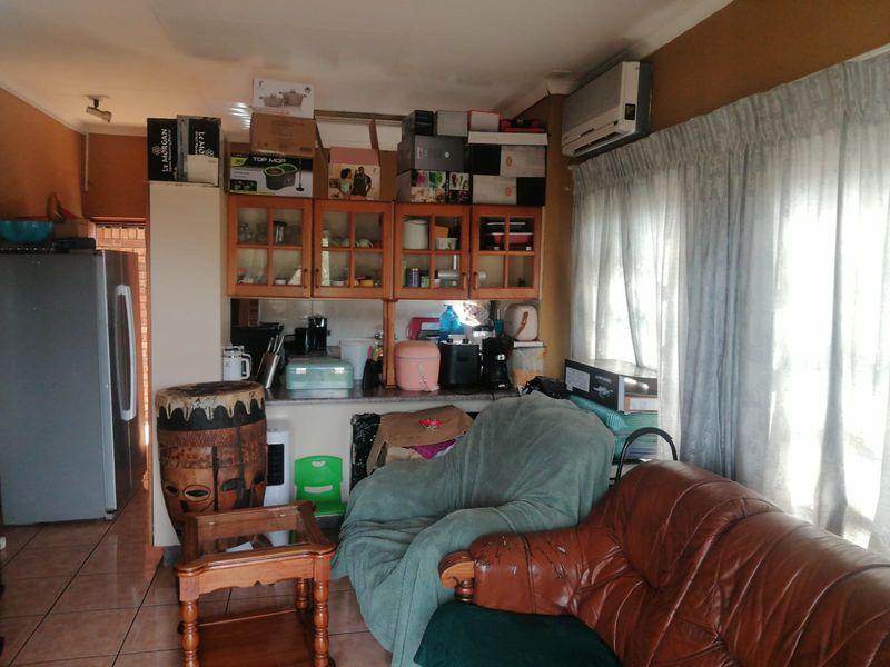 Open plan living and kitchen area featuring tiled flooring, built-in cabinetry, and an air conditioning unit, requiring cosmetic updates to improve the overall aesthetic.