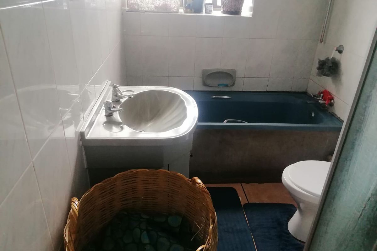 A functional bathroom featuring a pedestal basin, built-in bathtub, and toilet with full-height wall tiling, requiring cosmetic updates to modernize the space.
