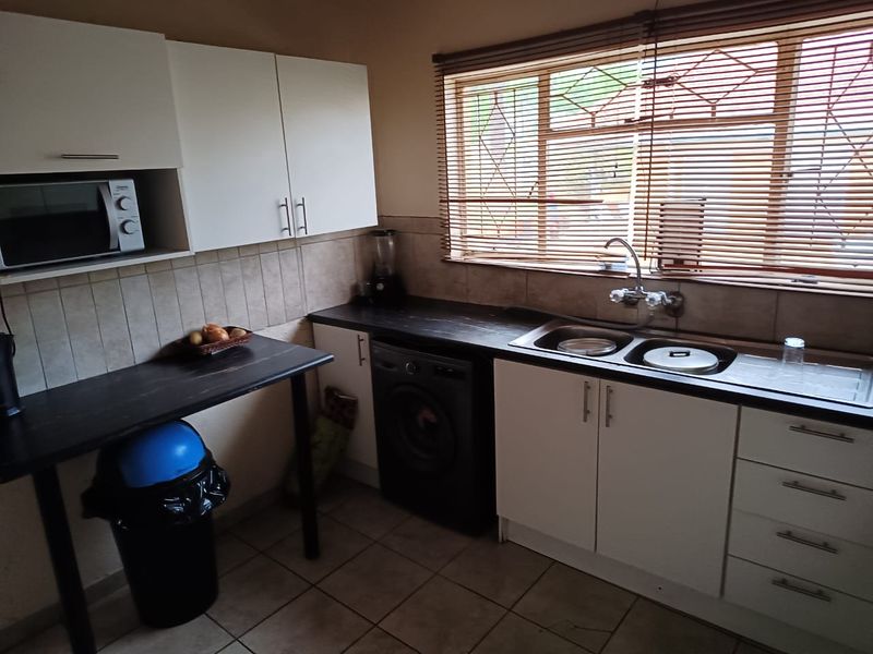 A functional kitchen featuring white cabinetry, dark laminate countertops, a double basin sink, and tiled flooring with a window overlooking the exterior.