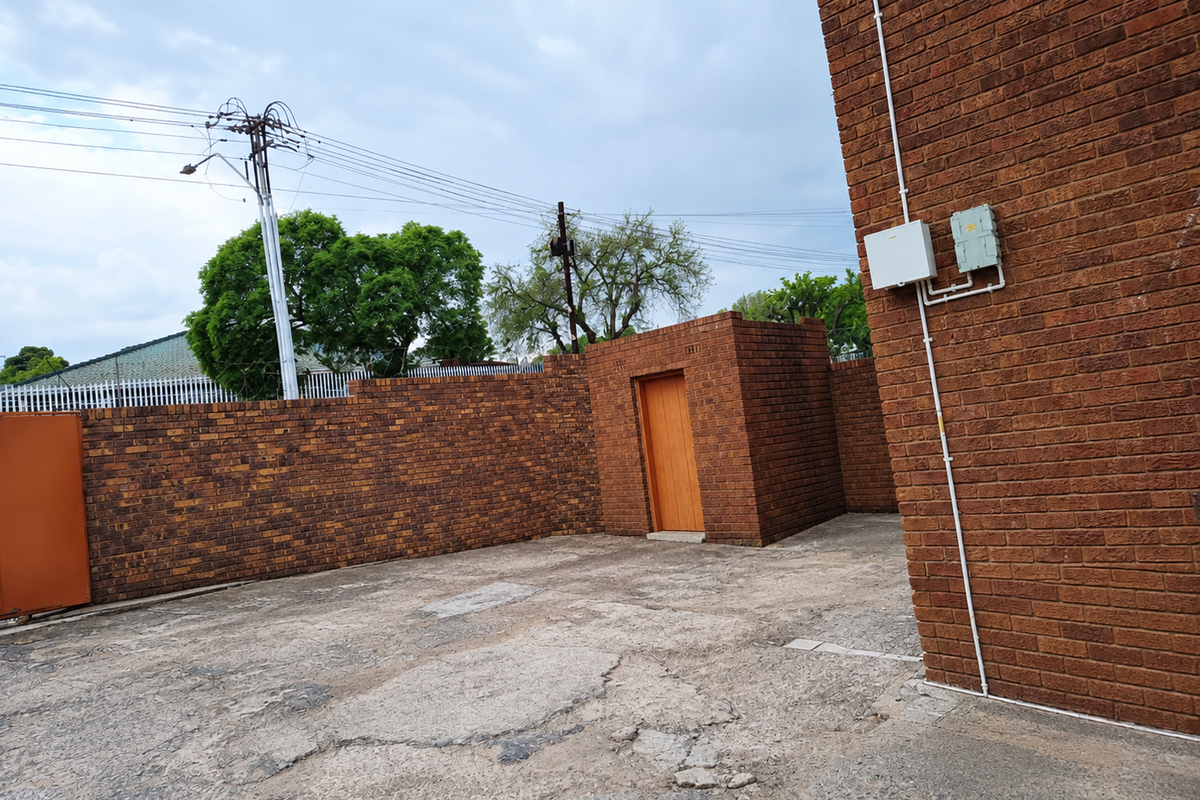 Rear courtyard area featuring brick boundary walls, a utility door, and weathered concrete paving with visible surface cracking.
