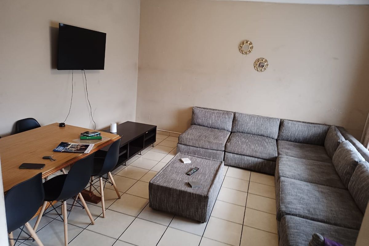 A living room featuring tiled flooring and coved ceilings, currently showing signs of wear on the wall surfaces.