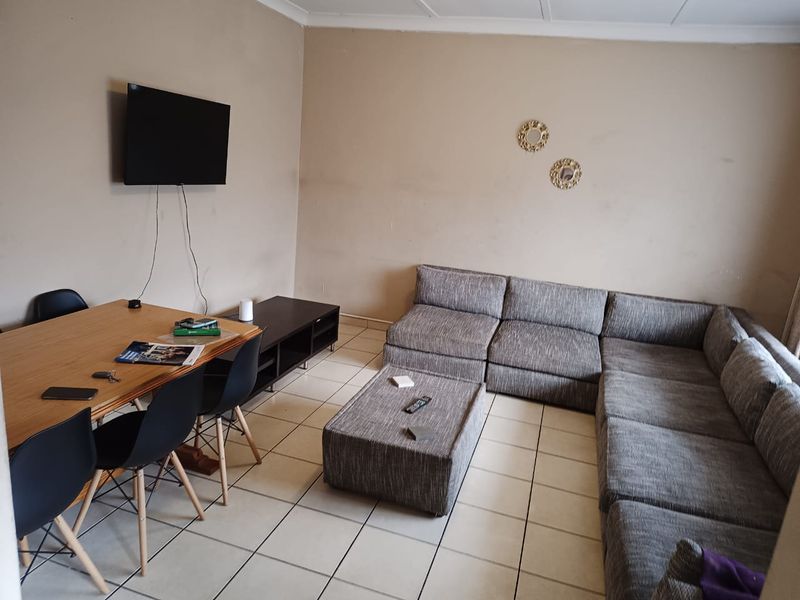 A living room featuring tiled flooring and coved ceilings, currently showing signs of wear on the wall surfaces.