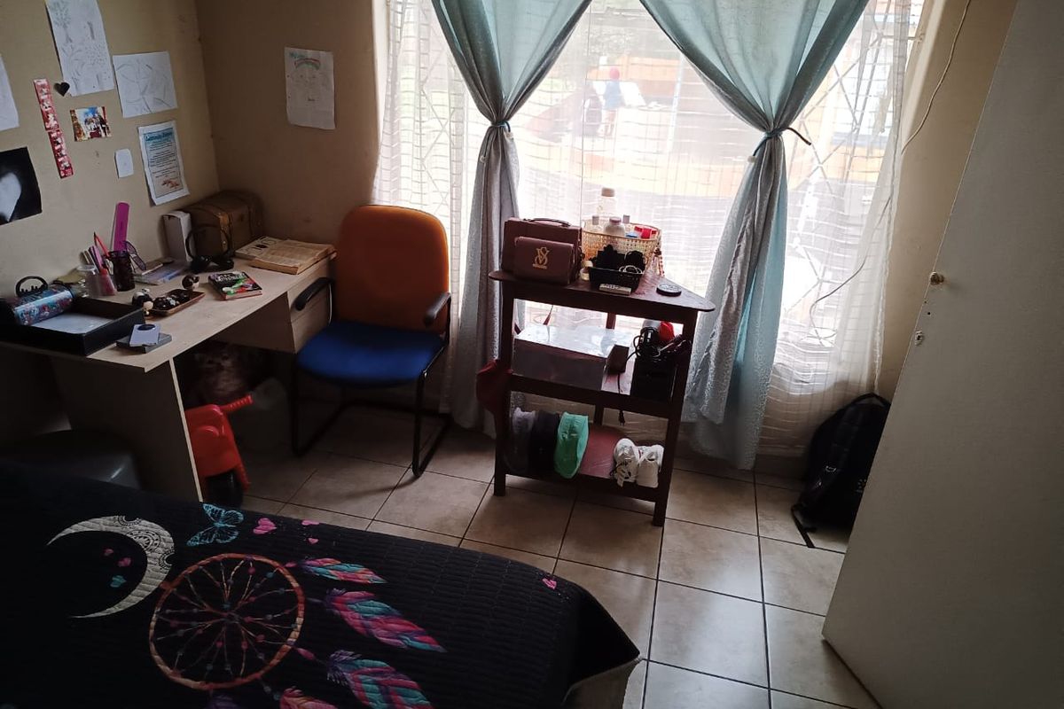 A bedroom featuring tiled flooring and a window fitted with security bars, providing natural light to the space.