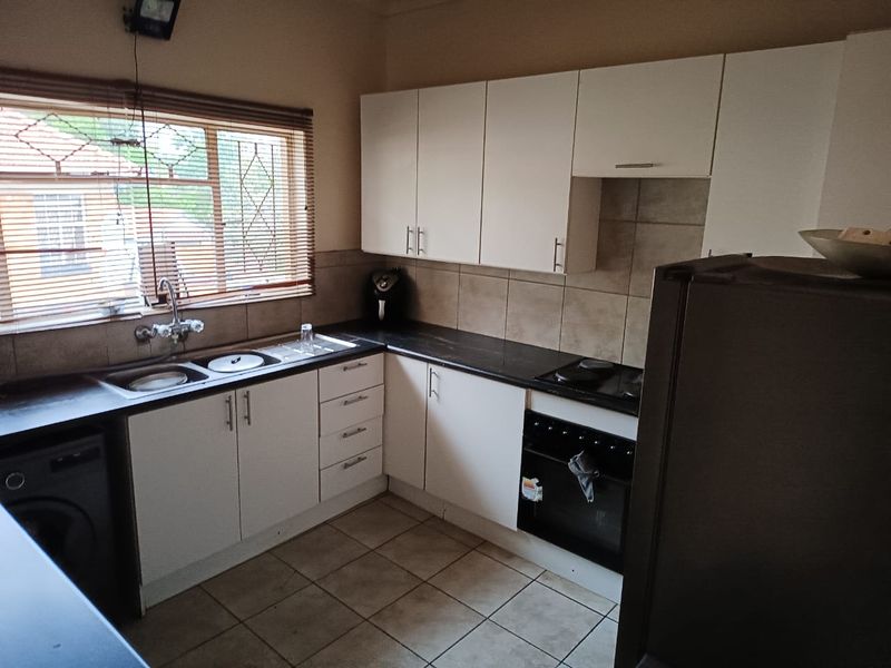 Functional kitchen featuring white cabinetry, dark laminate countertops, tiled backsplash, built-in oven, and hob, with tiled flooring and security bars on the window.
