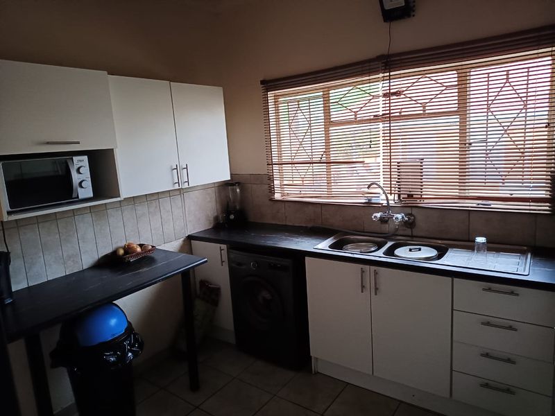Functional kitchen featuring white cabinetry, dark laminate countertops, a stainless steel double sink, and tiled backsplash with natural light from the window.