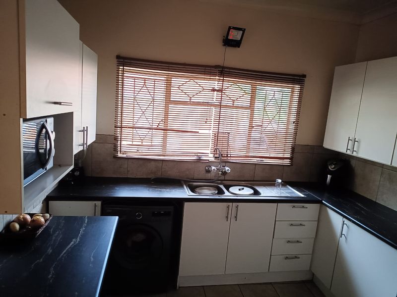 Functional kitchen featuring white cabinetry, dark laminate countertops, a double basin sink, and tiled backsplash with integrated appliance housing.