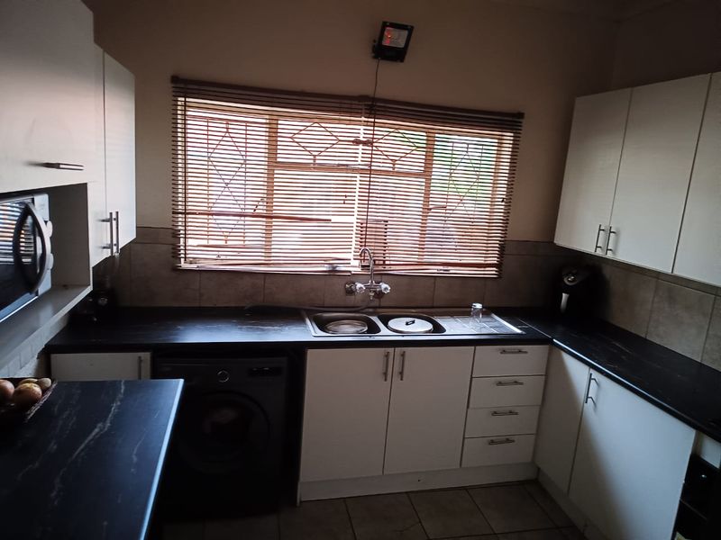 A functional kitchen featuring white cabinetry, dark laminate countertops, a stainless steel double sink, and tiled backsplash with natural light through a window.