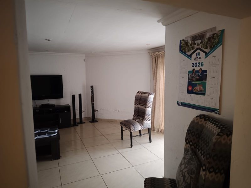 A living room area featuring tiled flooring and recessed lighting, currently showing signs of wear on the wall surfaces.